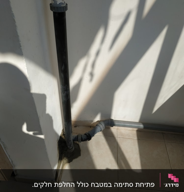 צינור ביוב שחור עם חיבורים על קיר לבן